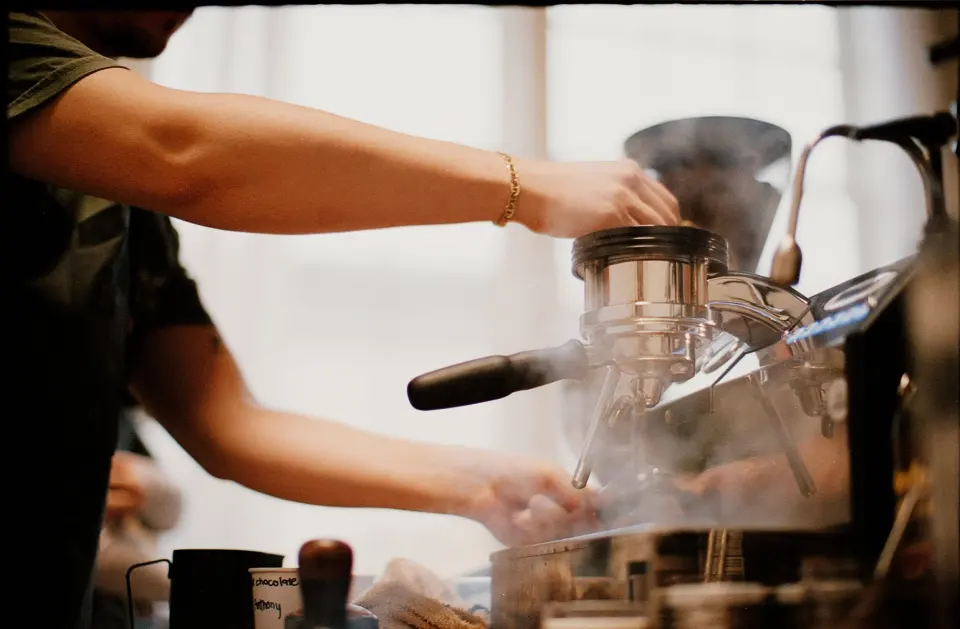 Steam rising off the espresso machine mid-pull, shot on film behind the bar